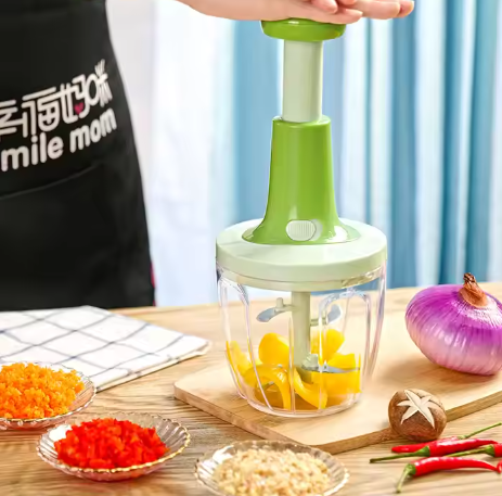 Green Souqzila handheld food chopper chopping yellow vegetables on wooden board with onion and spices nearby